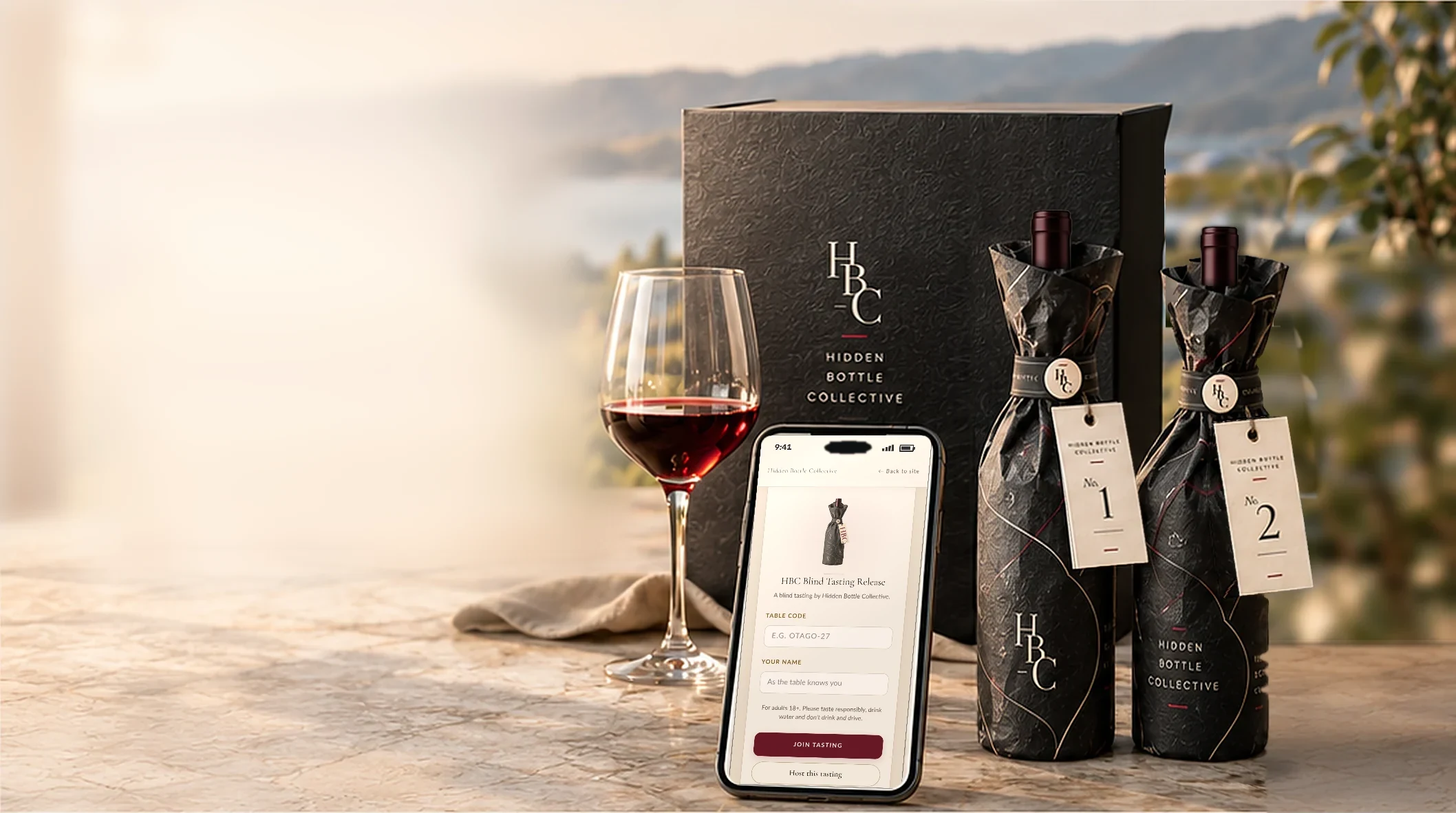 A Hidden Bottle Collective release: the graphite box, two wrapped bottles numbered 1 and 2, a glass of red wine and a phone showing the HBC Join Tasting screen