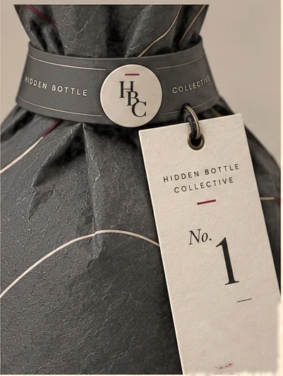 The shoulder band, HBC seal and numbered tag on a wrapped Hidden Bottle Collective bottle